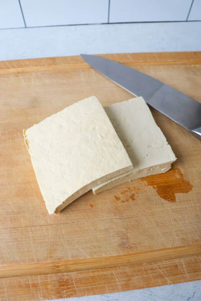 Tofu block cut in half on a cutting board.