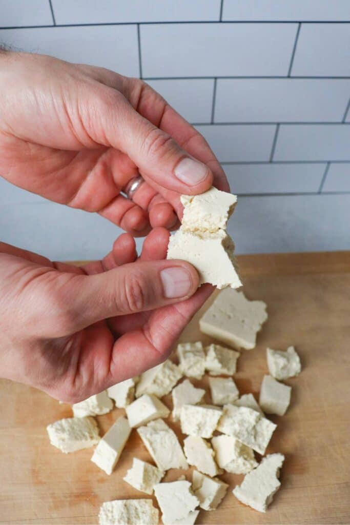 Hand tearing apart tofu into pieces.