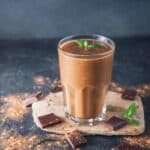 Thin mint smoothie topped with a piece of fresh mint in a glass next to squares of dark chocolate.
