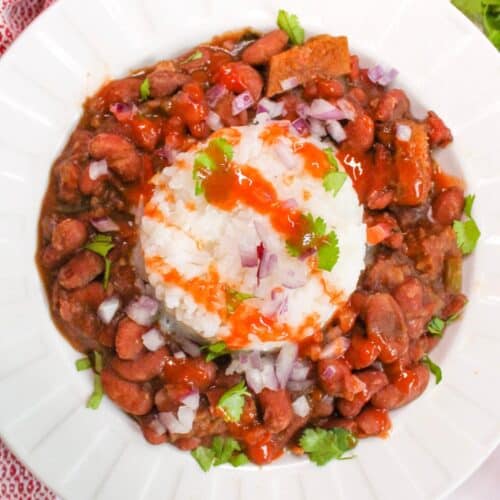 Overhead view of vegan red beans with white rice and topped with hot sauce and cilantro.