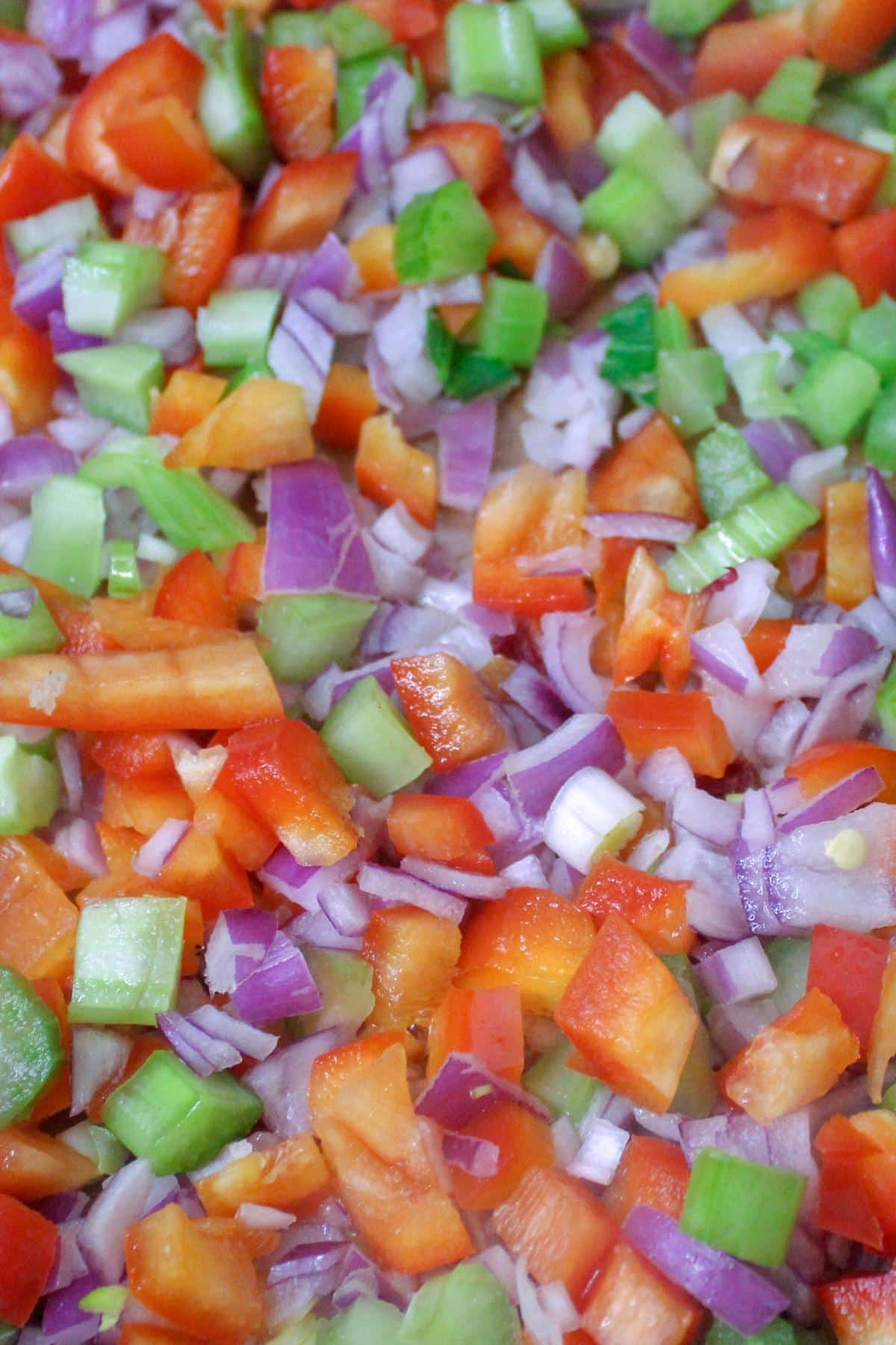 Close up image of onions, celery and bell peppers cooking in a pan. 