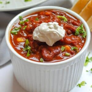 Vegan three bean chili in a small white bowl topped with sour cream.