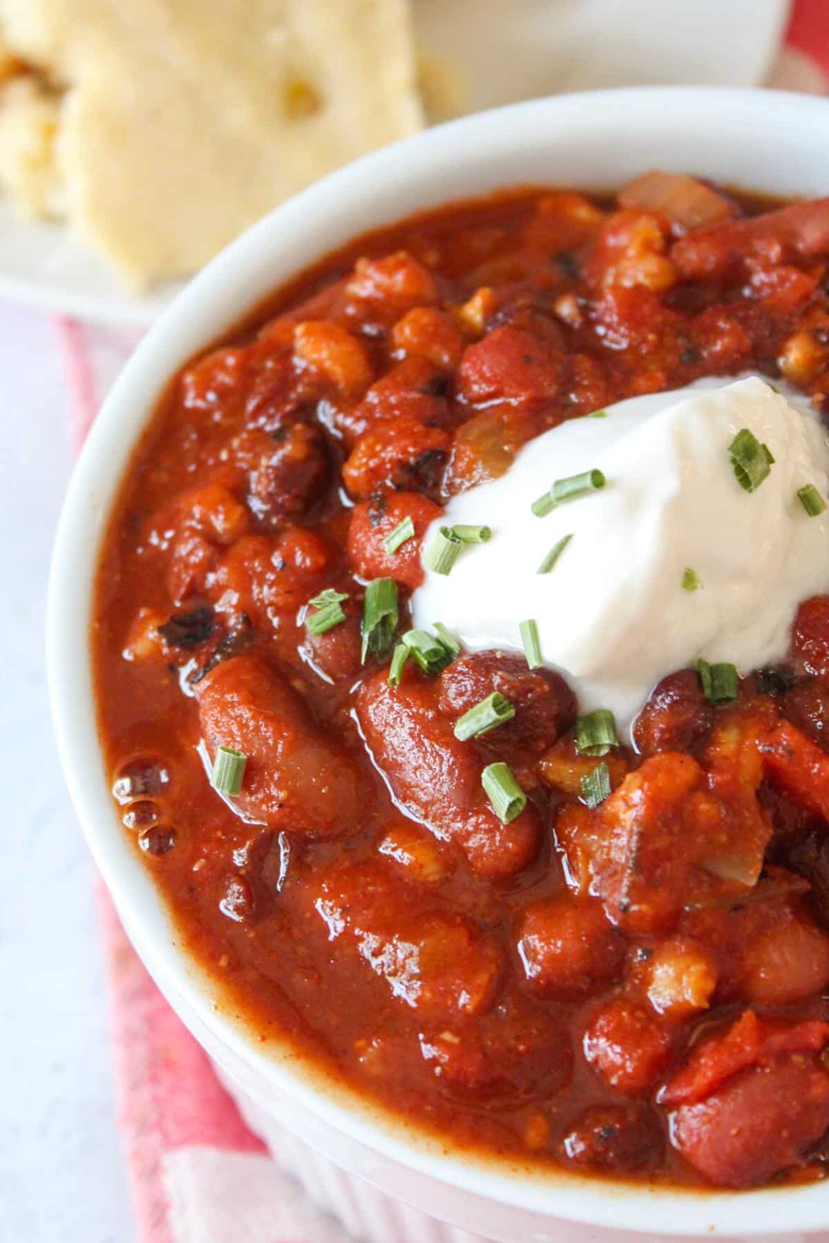 Close up view of vegan three bean chili in a bowl topped with sour cream.