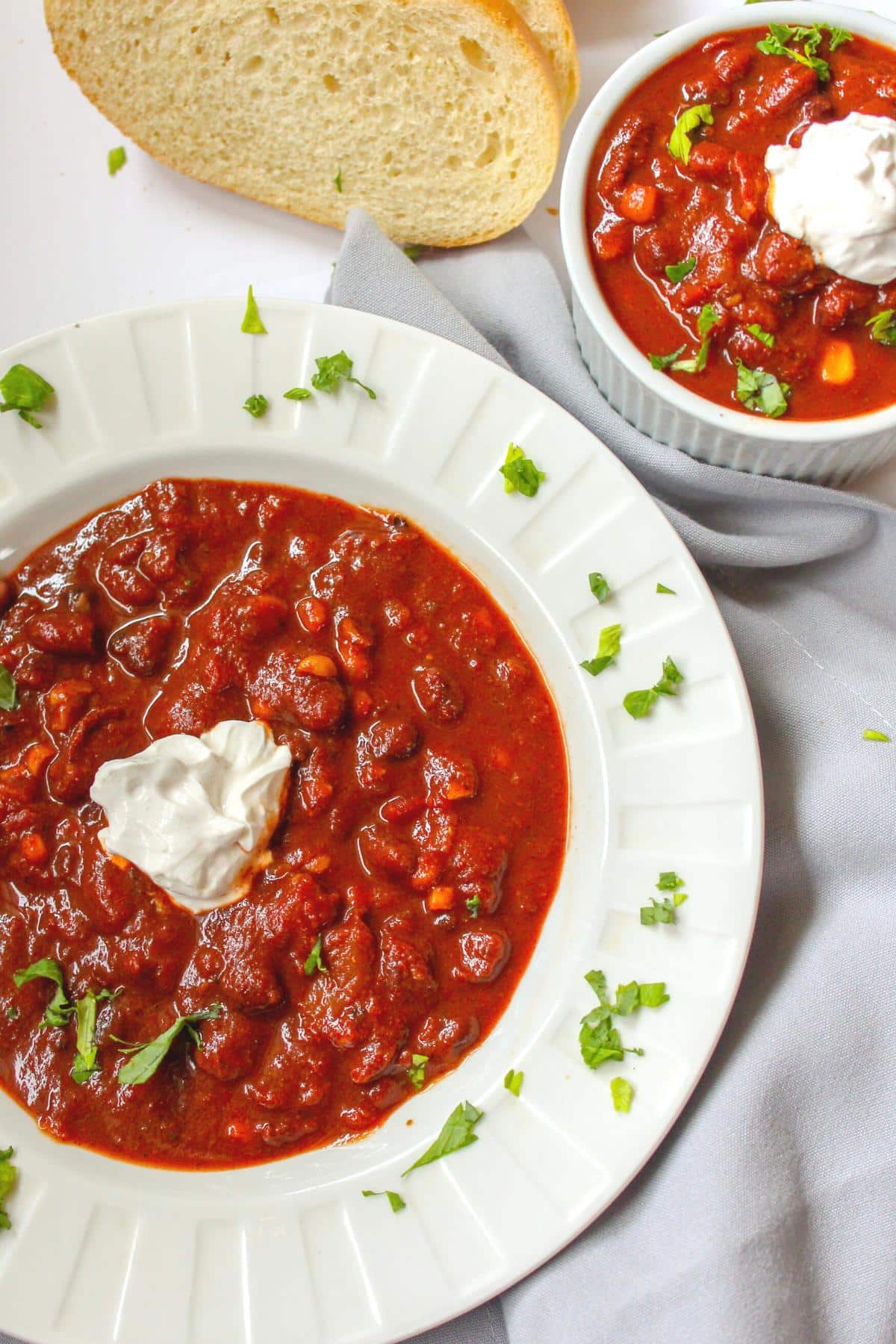Vegan three bean chili in a bowl topped with sour cream next to sliced bread.