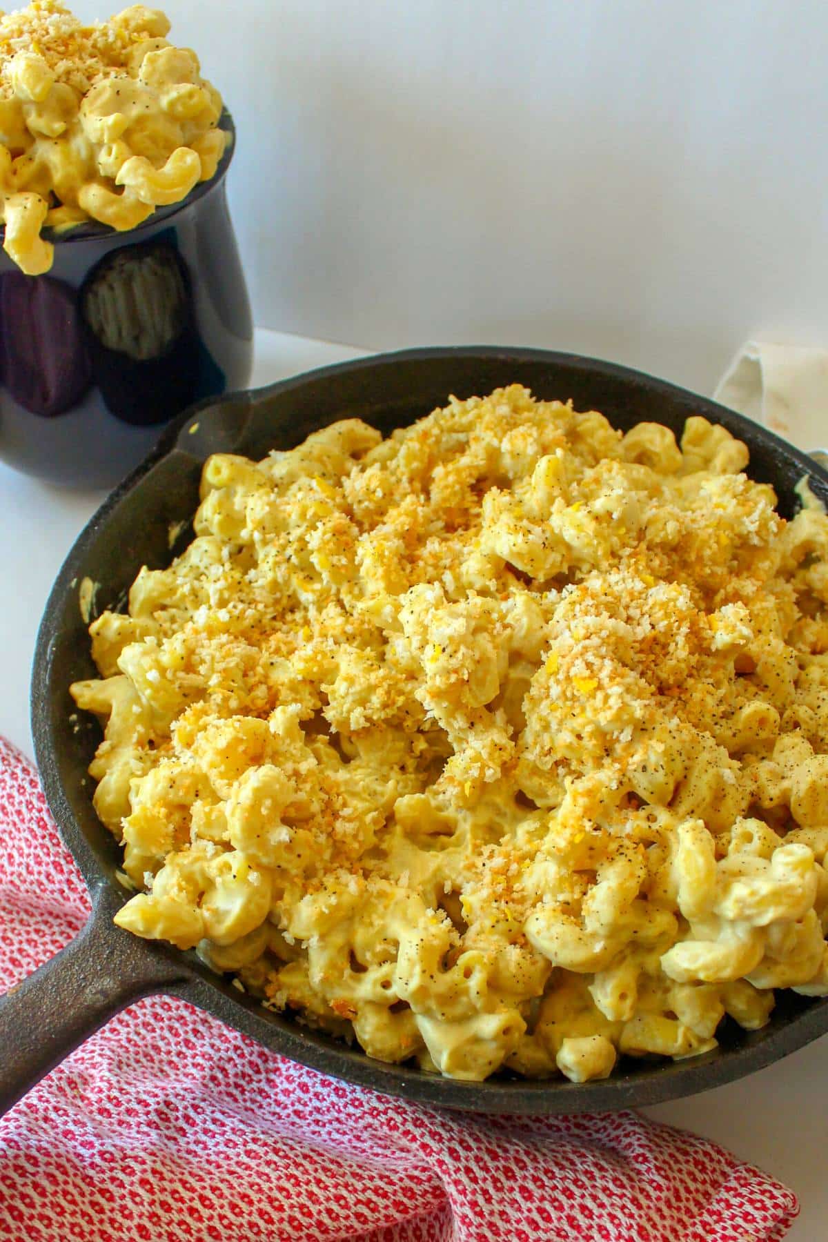 Vegan smoked gouda mac and cheese in a cast iron skillet next to a navy blue mug of the same thing.