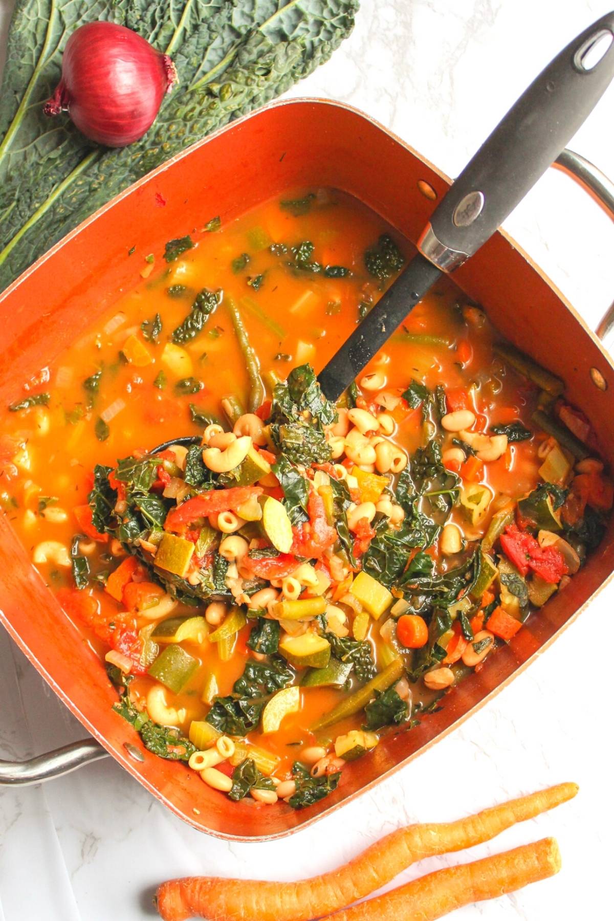Vegan minestrone soup in a large soup pan with a ladle.