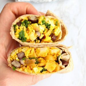 Hand holding a vegan breakfast burrito cut in half