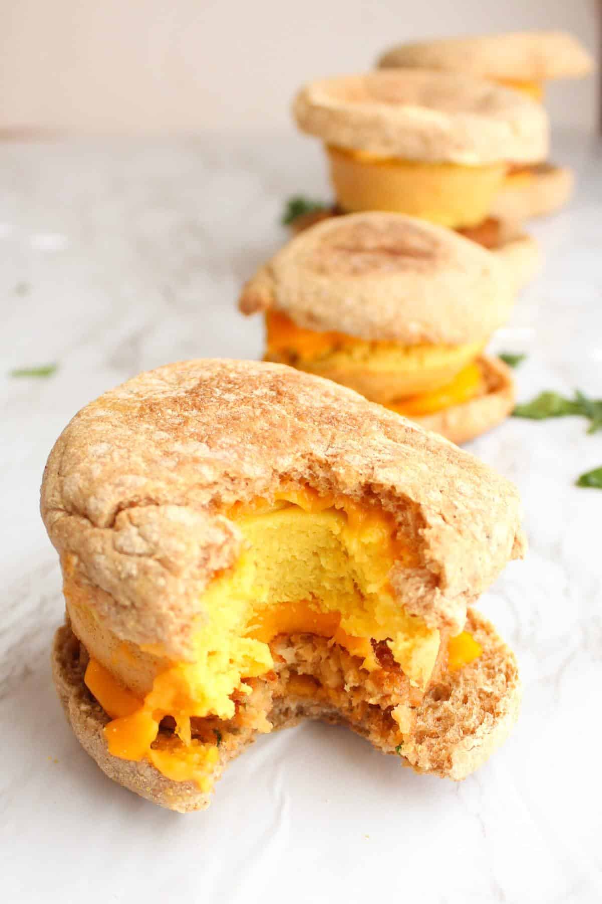 Three vegan breakfast sandwiches on a counter with a bite taken out of the one in front.