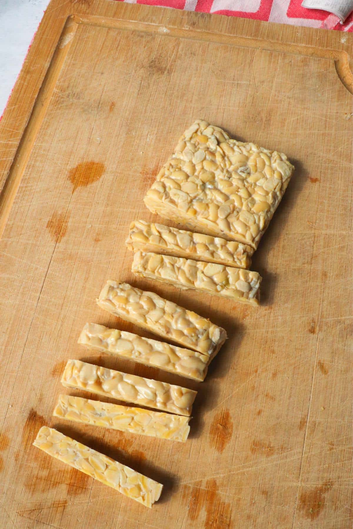 Block of tempeh cut into strips on a wooden cutting board.