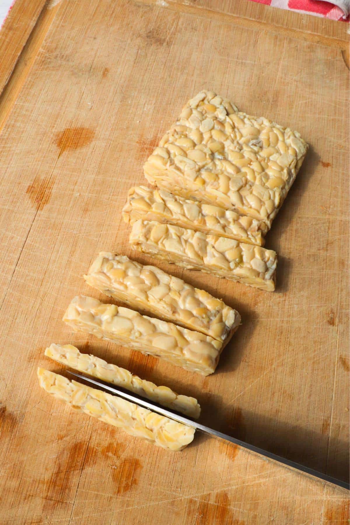 Block of tempeh strips being cut in half on a cutting board.