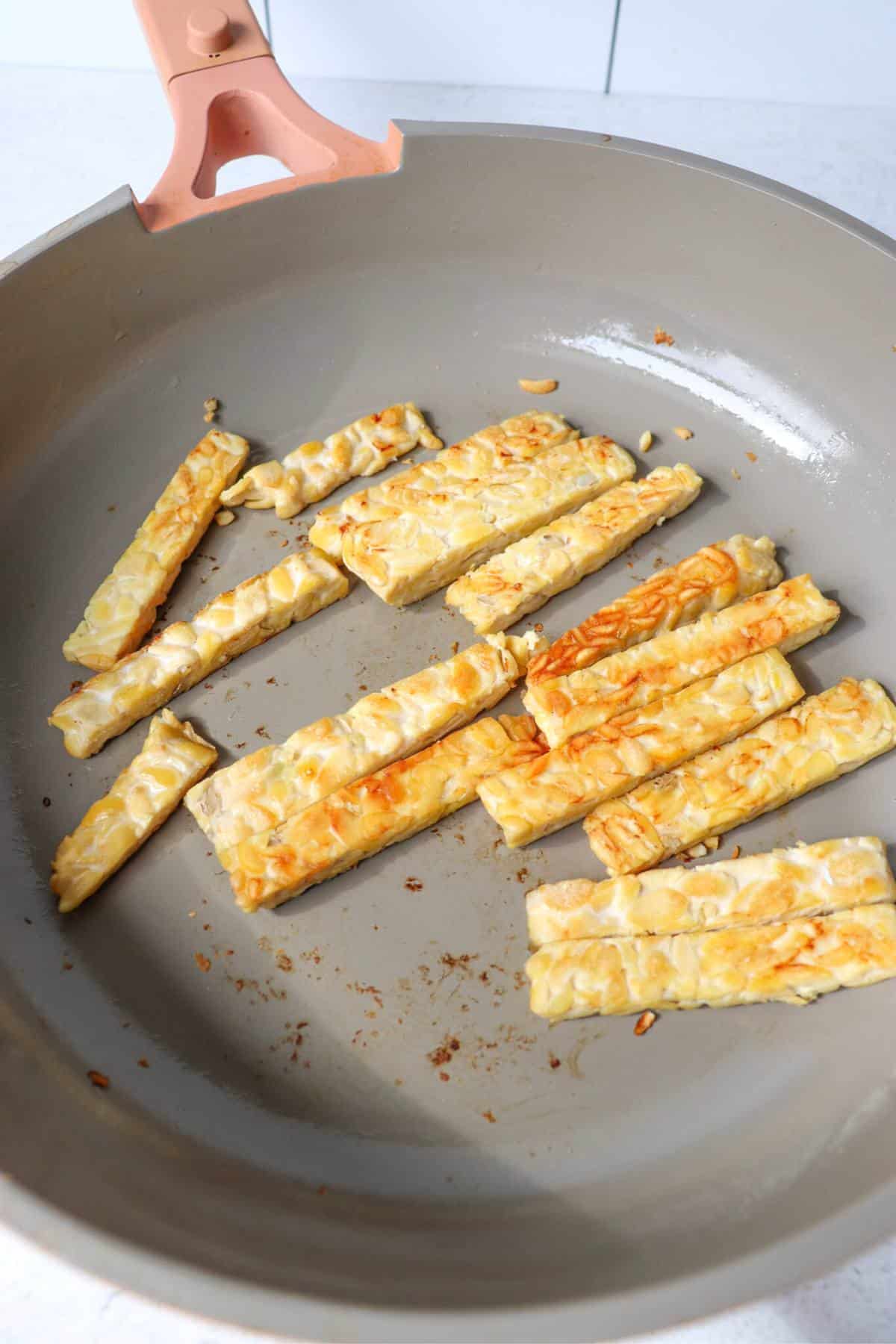 Tempeh strips being pan fried.