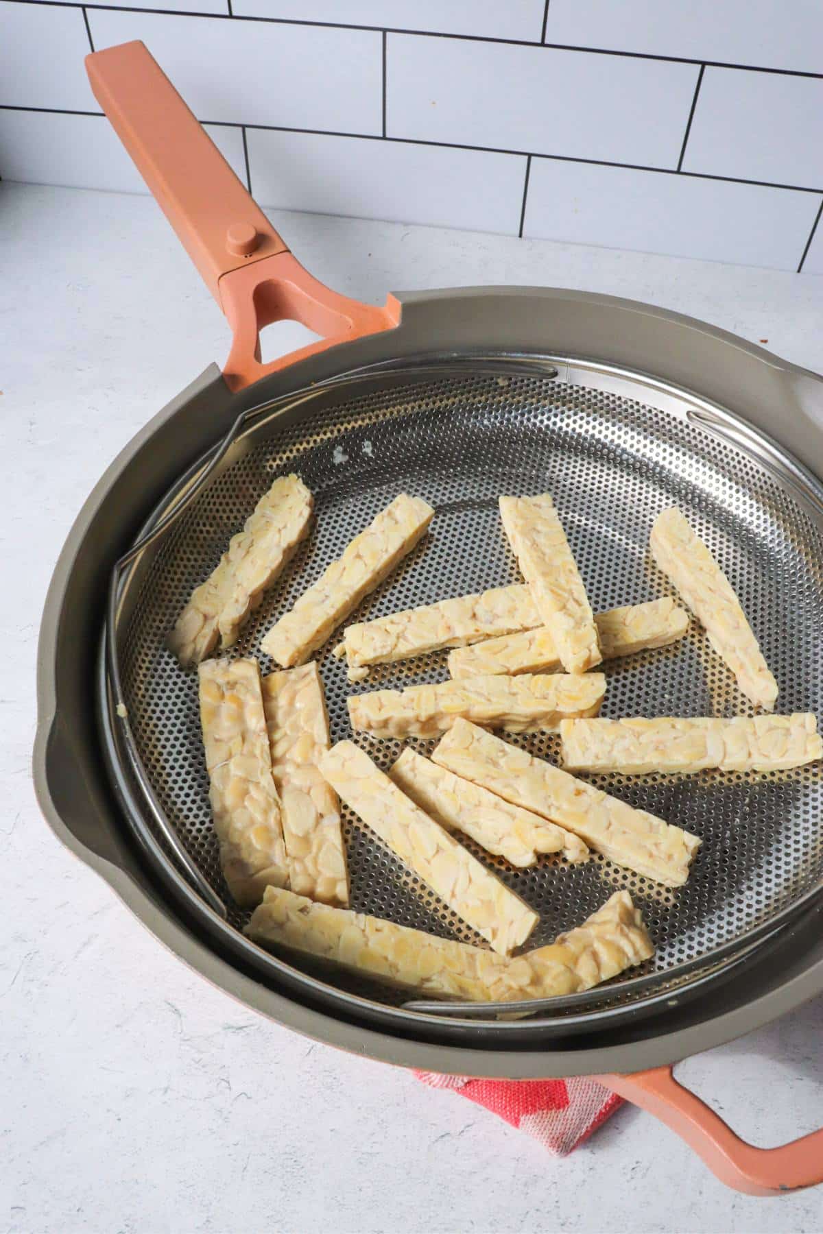 Tempeh strips being steamed in a steamer basket.