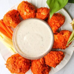 Buffalo cauliflower on a plate with vegan ranch, celery and carrot sticks