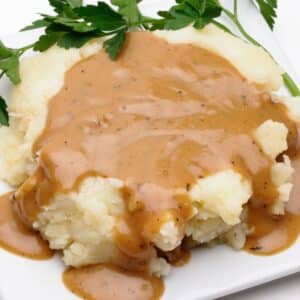 A plate of mashed potatoes with brown gravy dripping off of it.