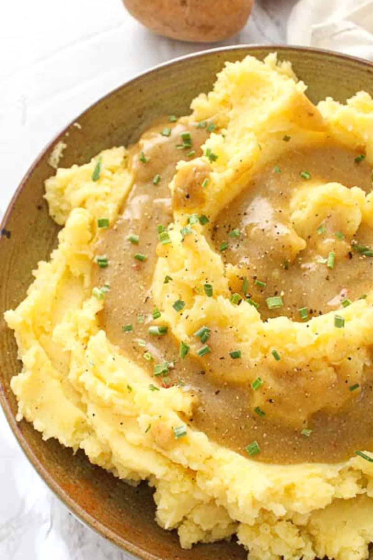 Big serving bowl of mashed potatoes drizzled with vegan brown gravy.