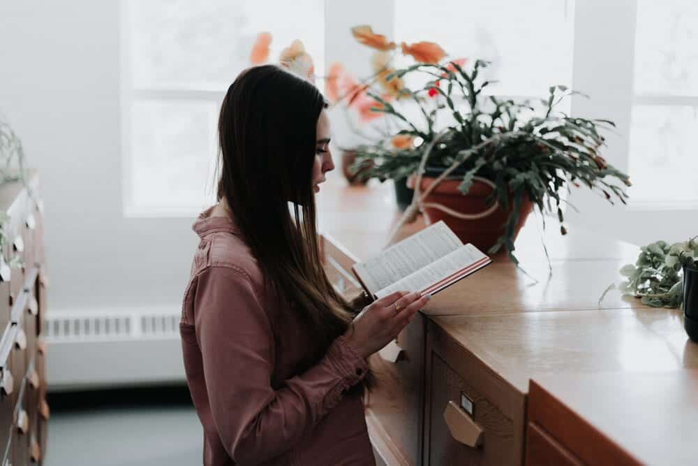 Woman standing in a a brightly lit room reading a book.