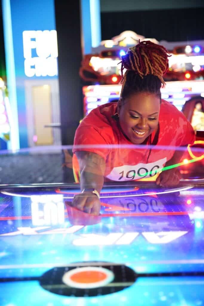 Woman smiling while playing air hockey at an arcade. 