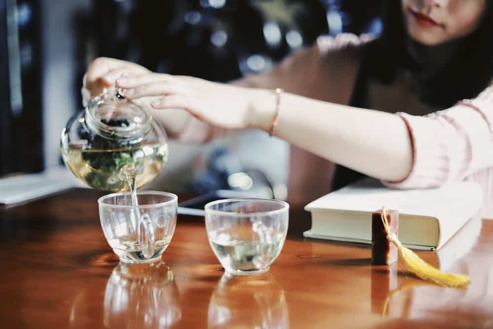 Loose leaf tea in a glass tea pot getting poured into glass mugs.