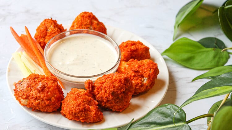 Plate of buffalo cauliflower with vegan ranch dressing, carrot sticks and celery.