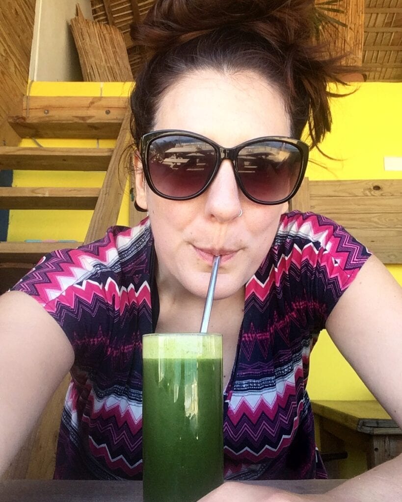 Woman with sunglasses sipping a green juice with a straw.