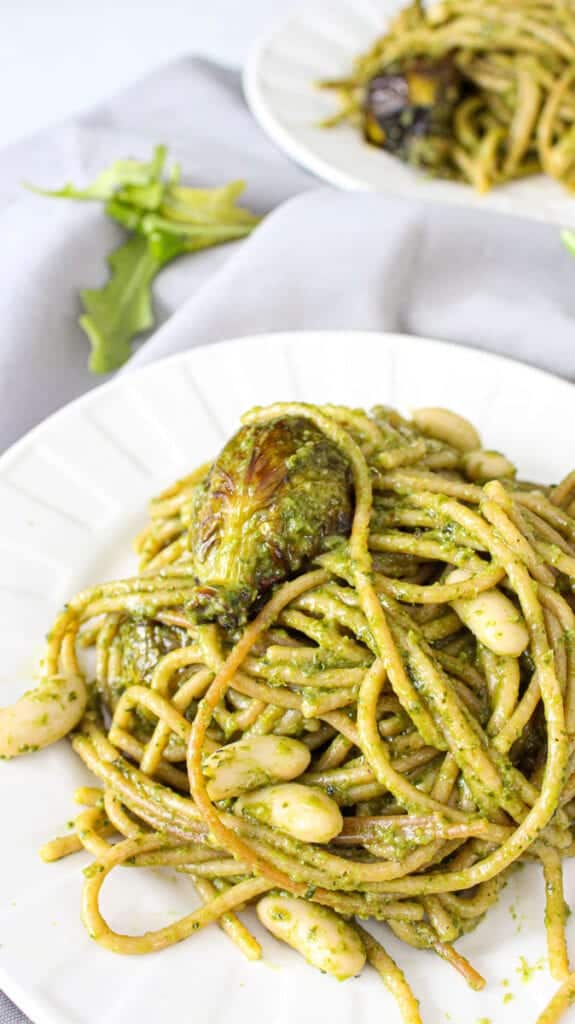 Pesto pasta on a white plate with roasted brussels sprouts