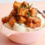 Sticky glazed maple miso tofu in a pink bowl on top of rice.