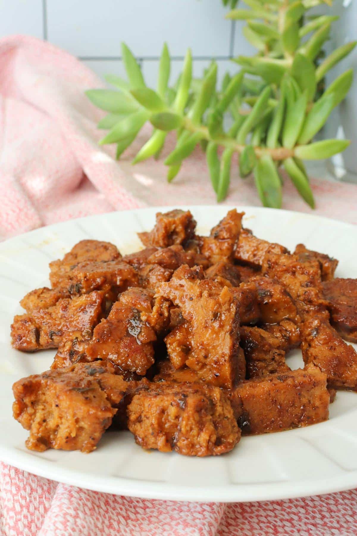 Small pieces of marinated and sautéd seitan on a white plate.