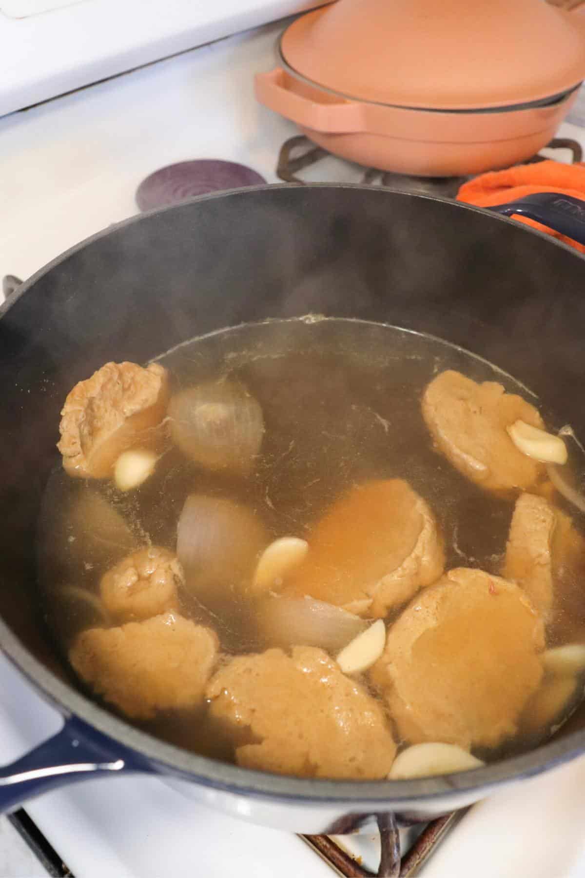 Seitan pieces simmering in a broth on the stove.