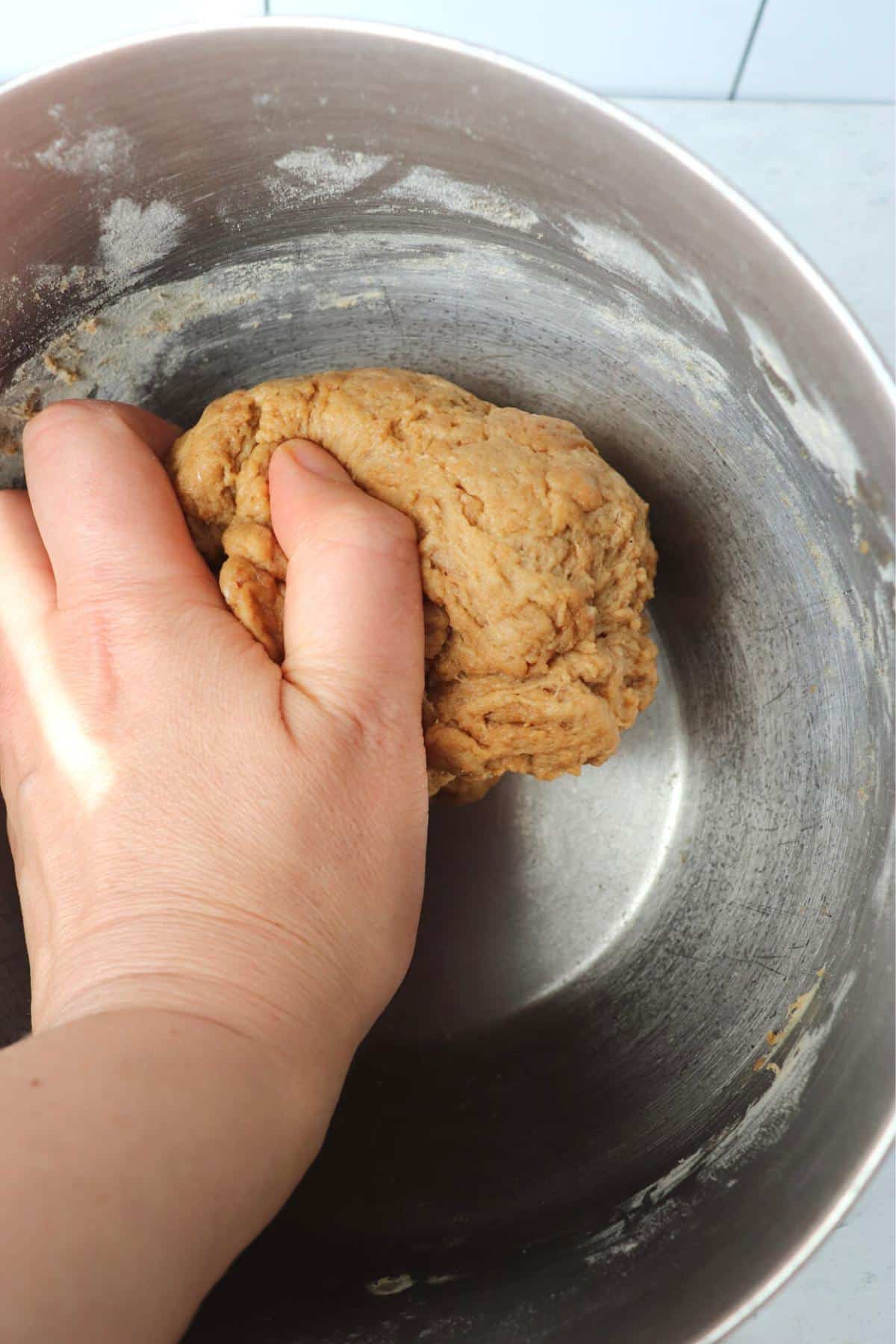 Hand kneading a ball of seitan dough in a mixing bowl.