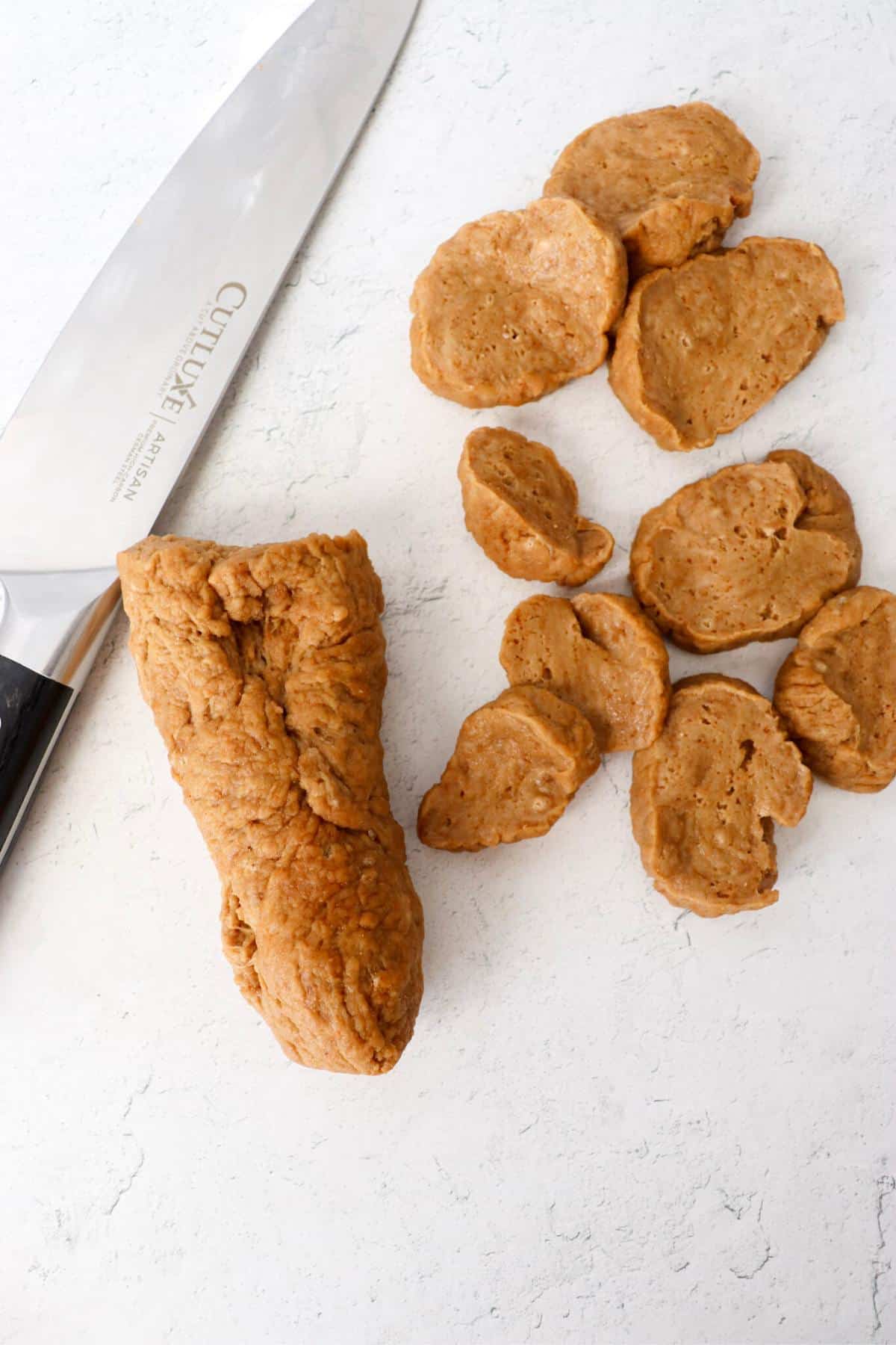 Seitan rolled into a log and cut into rounds, next to a knife.