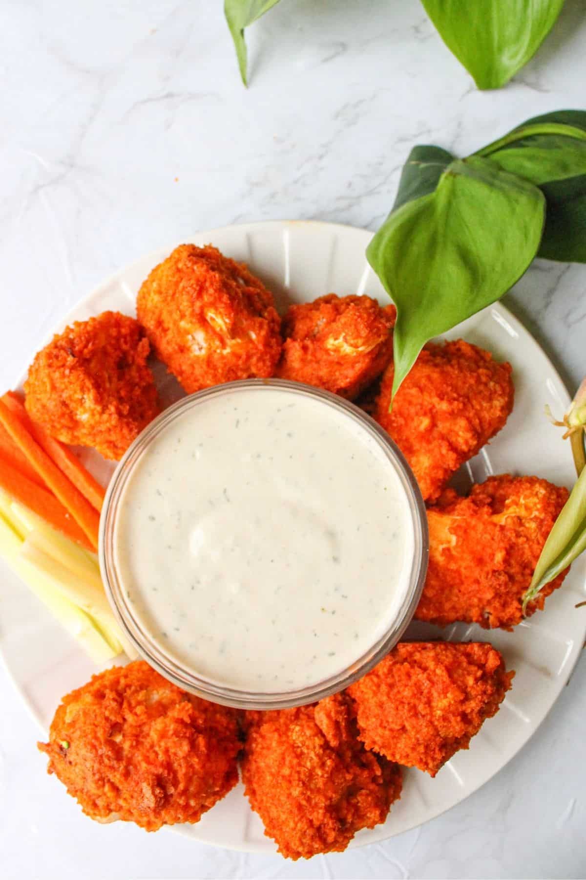 Crispy cauliflower wings on a plate with vegan ranch in the middle.