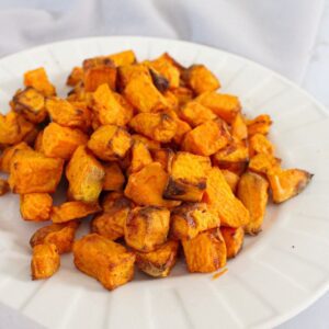 Sweet potatoes cubed and roasted and sitting on on a white plate