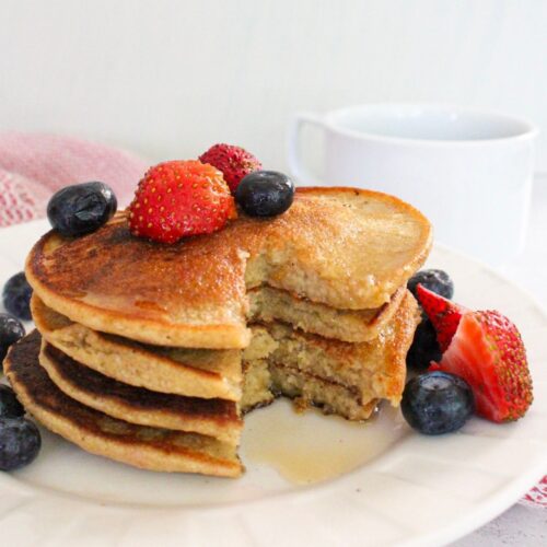 Stack of vegan pancakes with fresh berries and maple syrup.