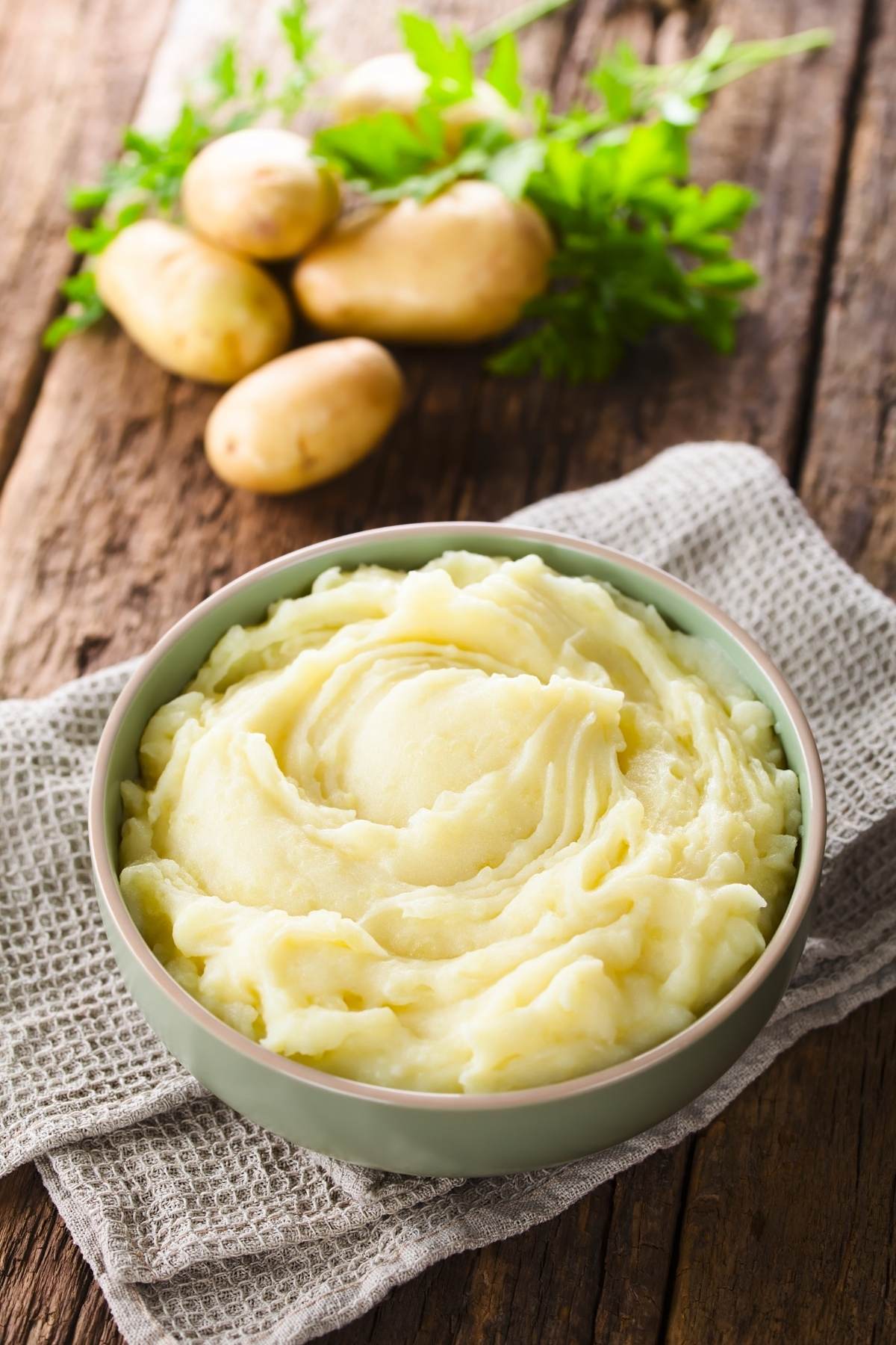 Bowl of creamy mashed potatoes without milk on a table with whole potatoes