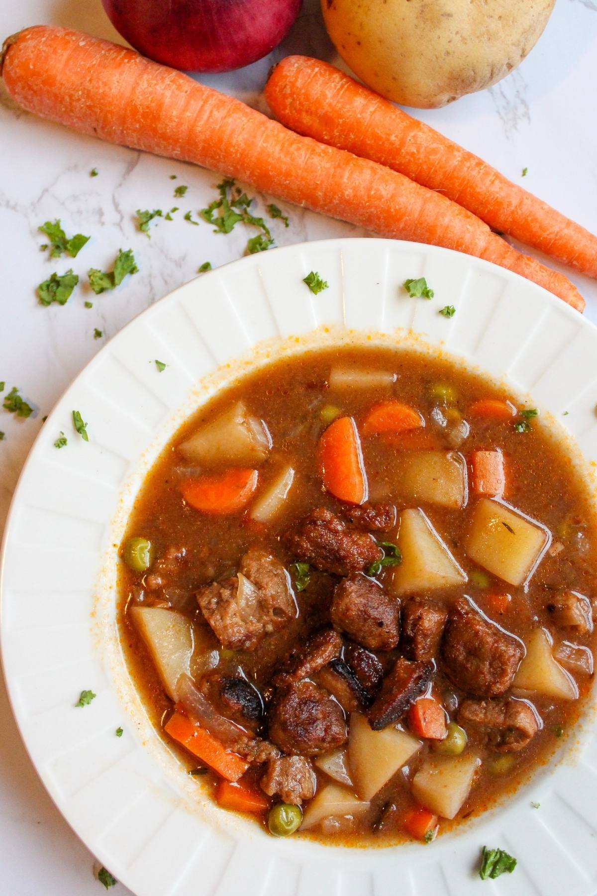 Bowl of vegan beef stew on a table with carrots.