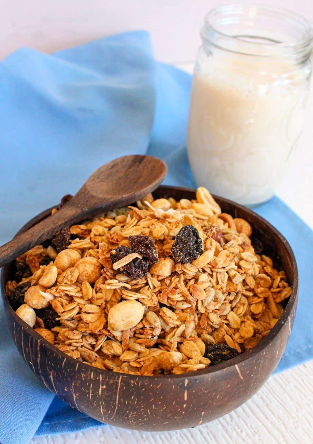 Vegan granola in a bowl with a wooden spoon and glass of milk