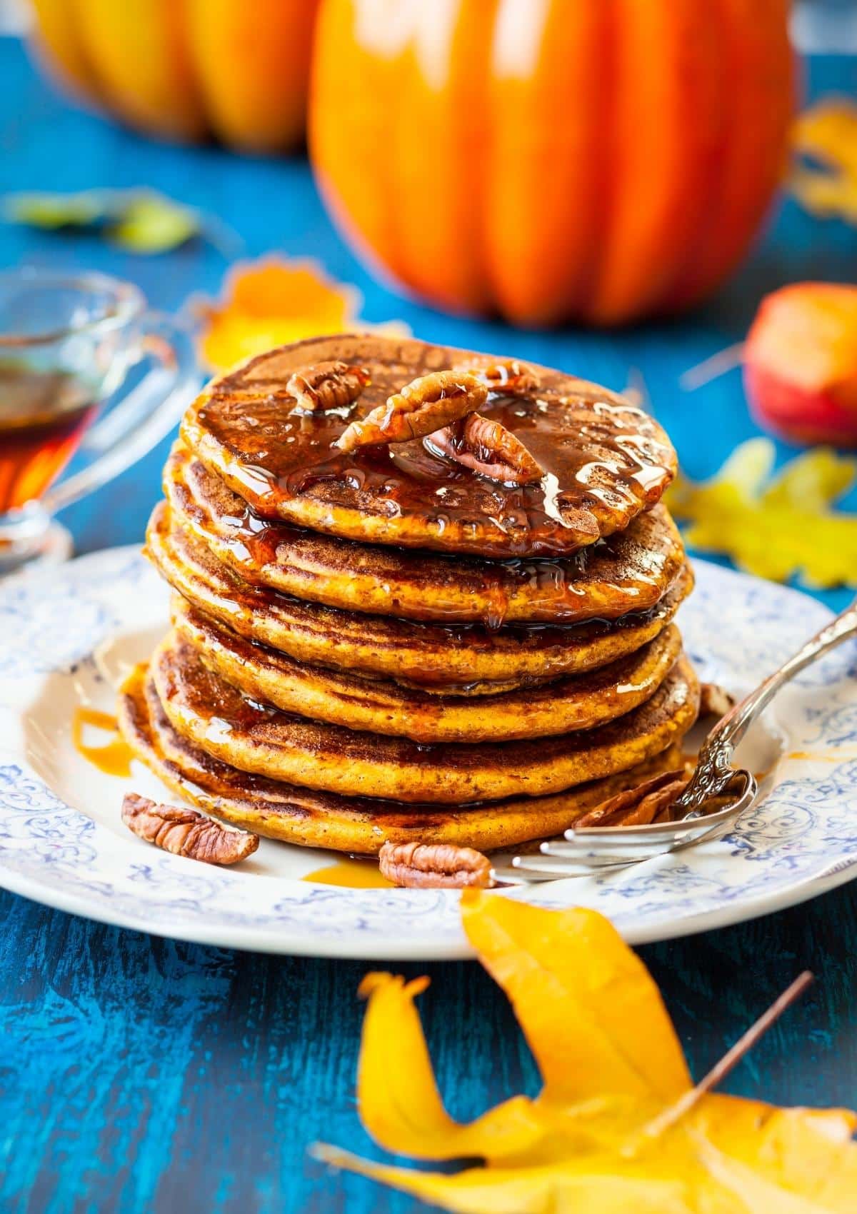 A stack of vegan pumpkin pancakes on a plate with maple syrup
