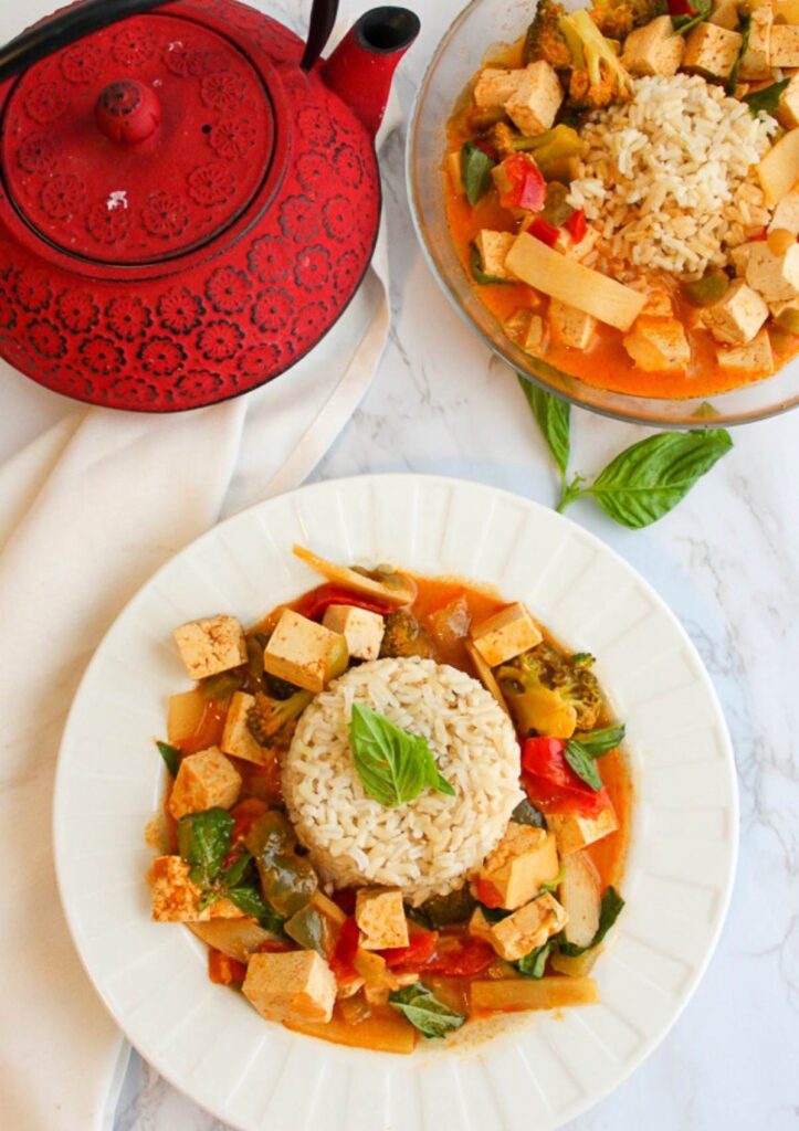Two white bowls of wegan red curry with tofu and vegetables, overhead view.