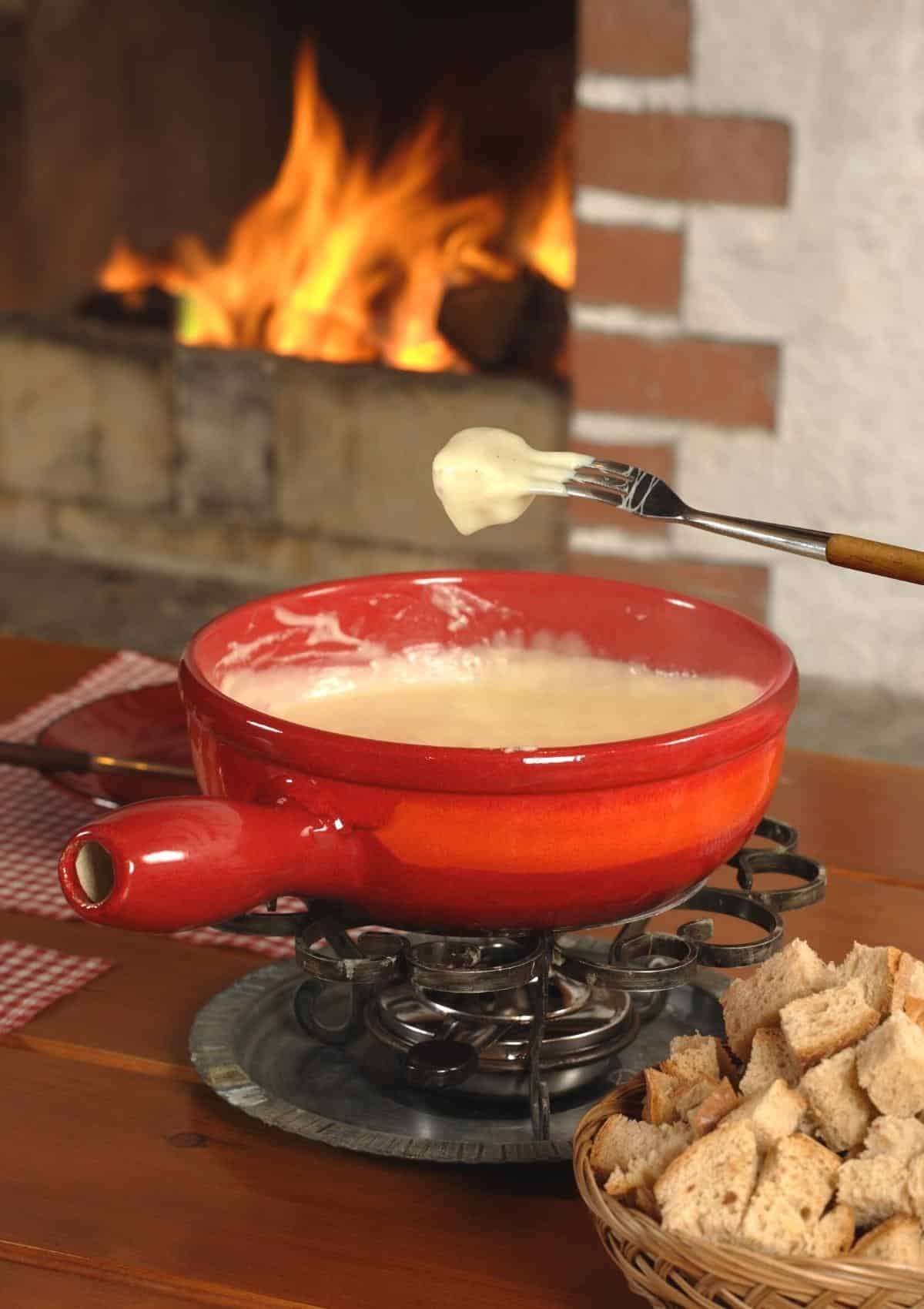 Fondue pot filled with vegan fondue and a piece of bread being dipped into it. 