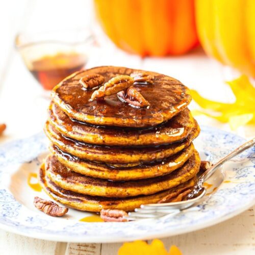 A stack of vegan pumpkin pancakes on a plate dripping with maple syrup