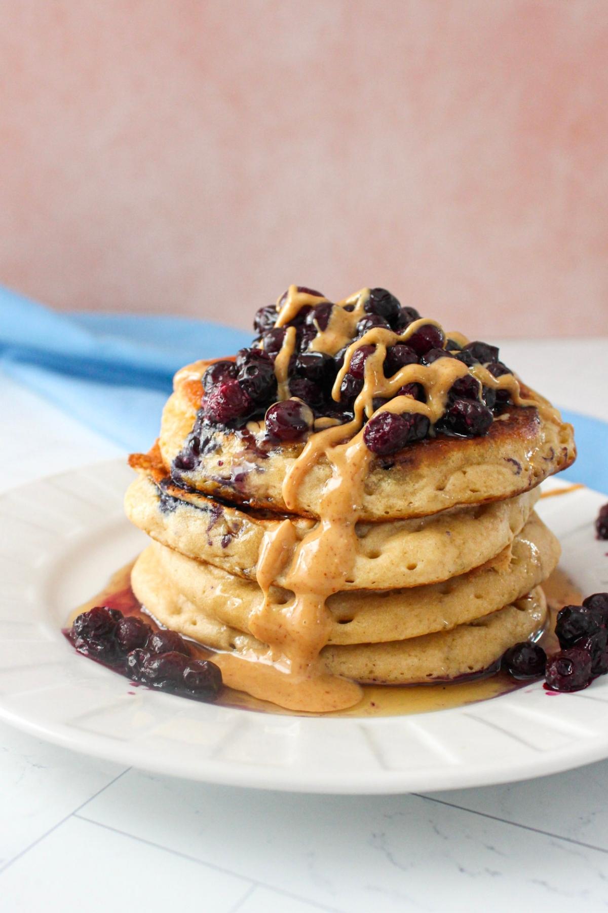 Stack of protein vegan pancakes on a plate topped with blueberries and peanut butter