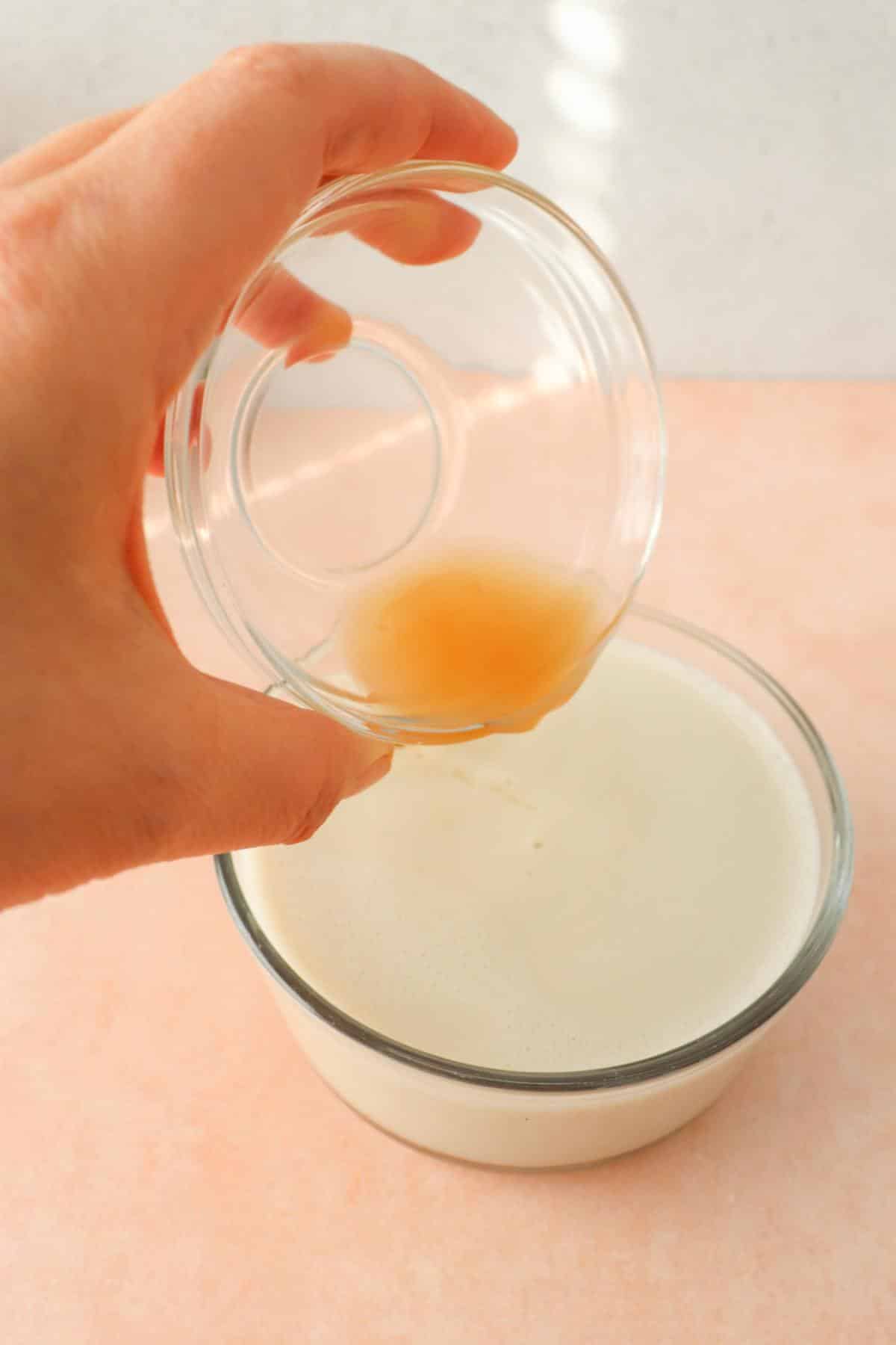 A hand pouring apple cider vinegar into soy milk to make vegan buttermilk.