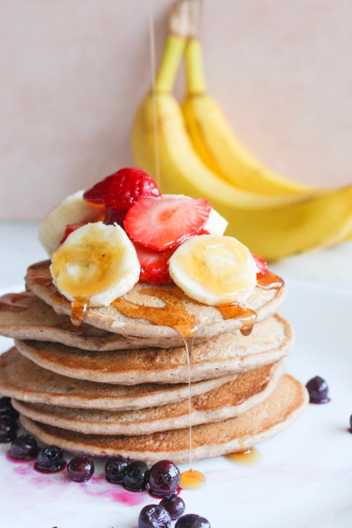 Stack of banana protein pancakes with syrup getting poured on them.