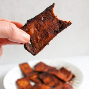 Hand holding a piece of tofu bacon