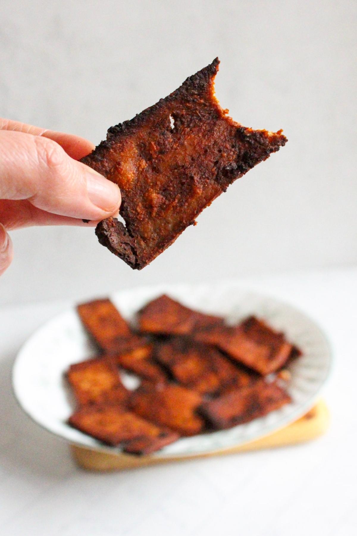 Hand holding a piece of tofu bacon