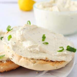 Tofu cream cheese spread out over a toasted bagel topped with green onions.