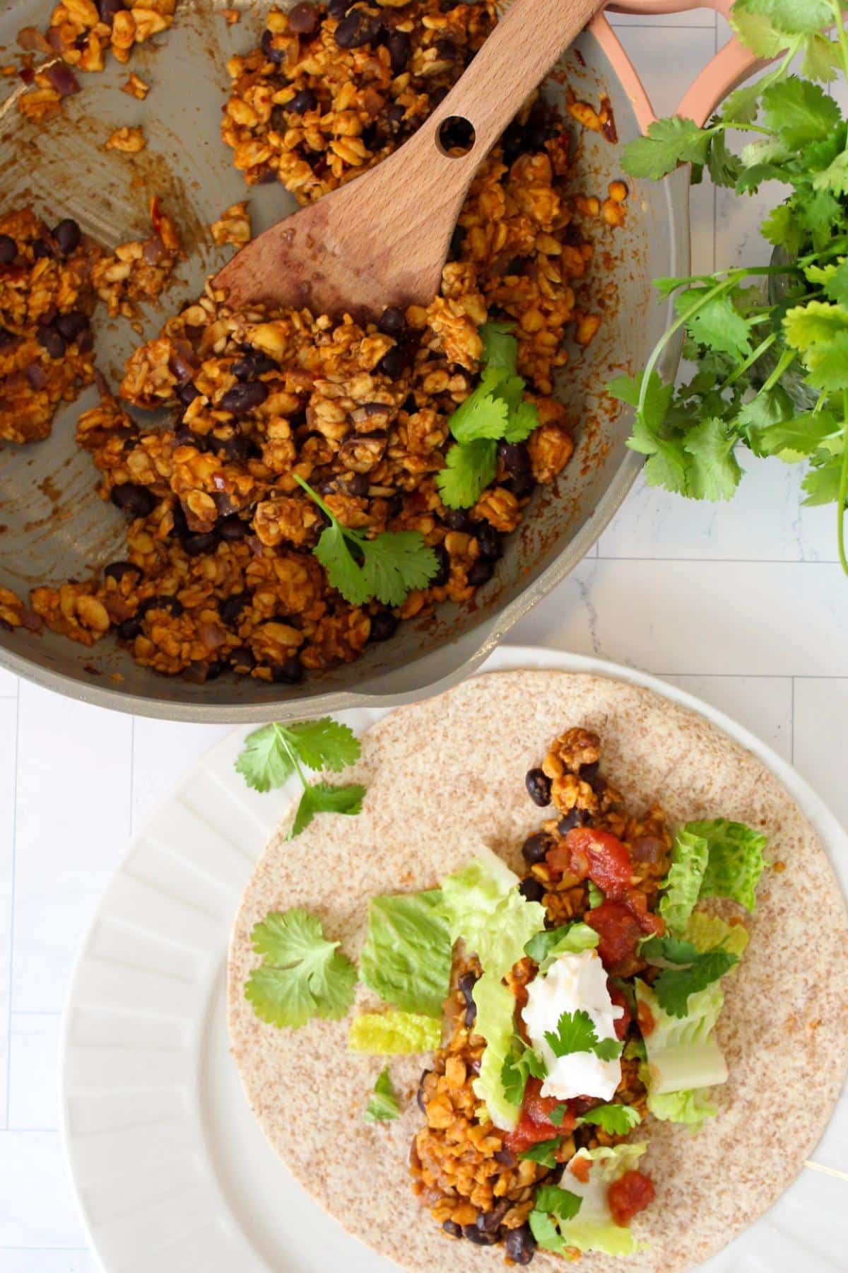 Overhead view of tempeh tacos on a plate next to a pan filled with tempeh taco stuffing.