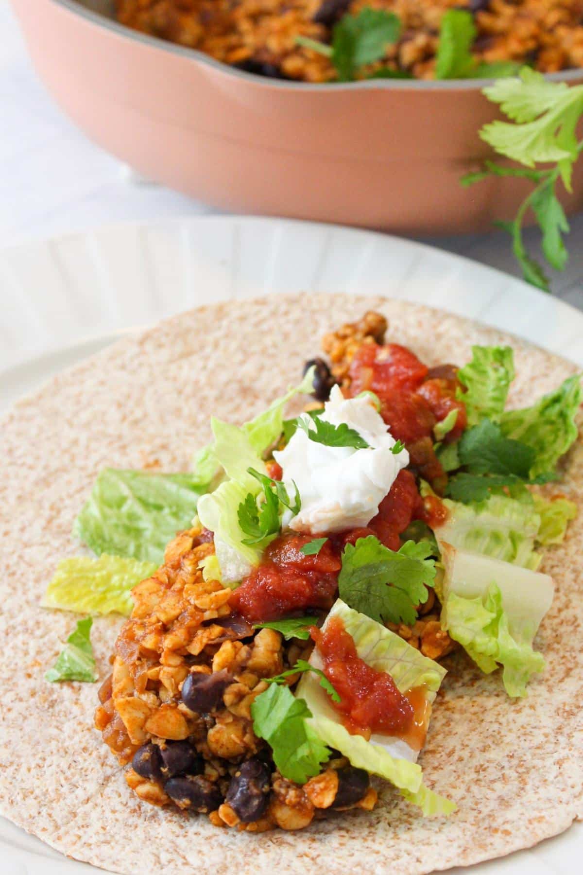 Vegan tempeh taco topped with lettuce, salsa and vegan sour cream.