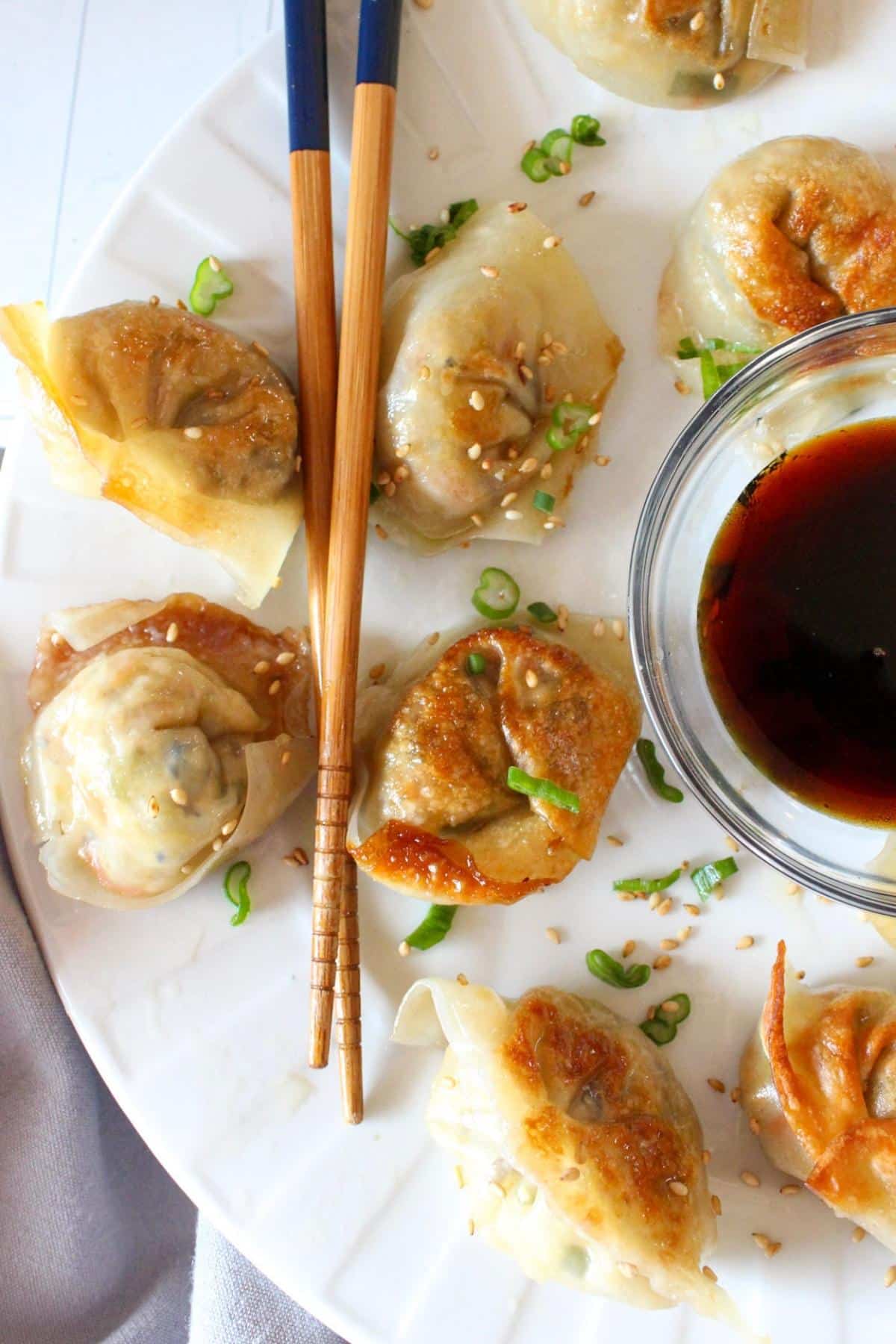 Plate full of vegan dumplings with chop sticks and soy sauce.