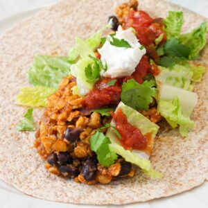 Tempeh taco on a plate topped with lettuce, salsa and dairy free sour cream.